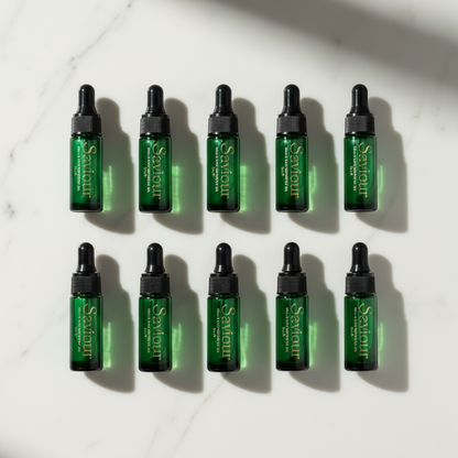 10 mini cuticle and skin oils, in green glass bottles on a white marble background